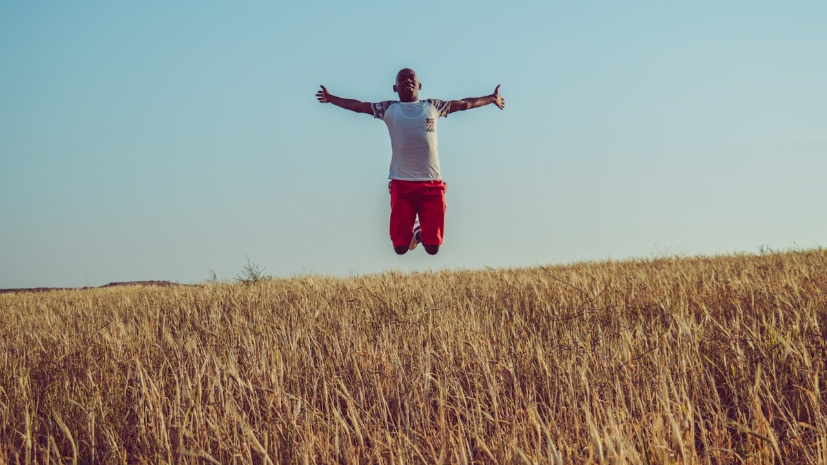 man in white shirt and red shorts jumping on brown grass field during daytime